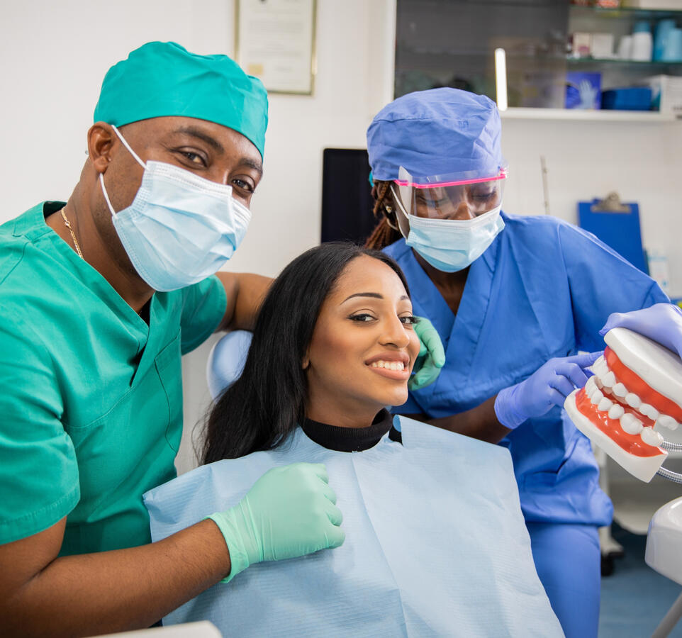 A young black woman, sitting in a dental chair with two dentists beside her.