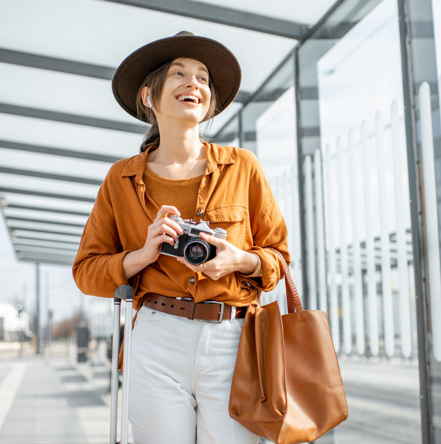 A young white woman, smiling holding a camera walking through the airport.