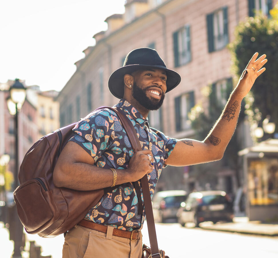 A young black man carrying a backpack waving down a cab.