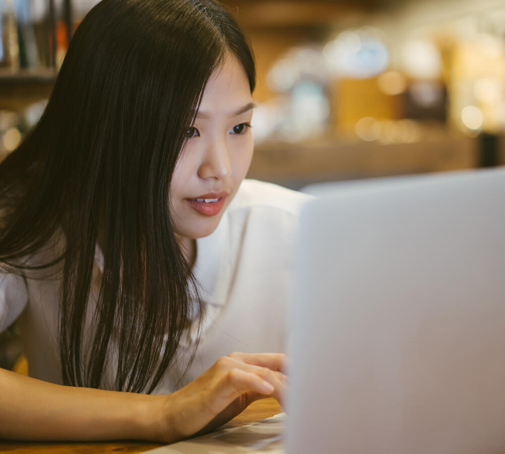 Young Asian girl looking into the screen of a laptop.